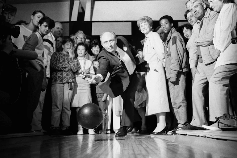 Neil Kinnock bowling while members of the public watch.