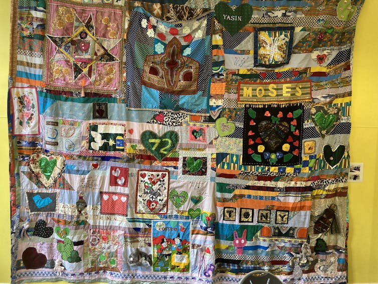 A large patchwork quilt with decorative elements in many colours, against a yellow wall.