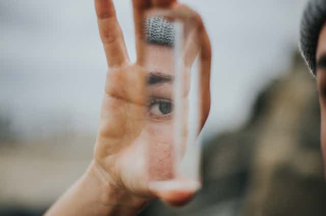 An experimental photo of a person's hand with a sliver of a mirror reflecting the person's eye. 