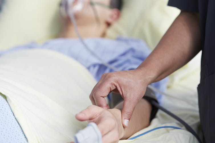 Doctor checks pulse of man in hospital bed.