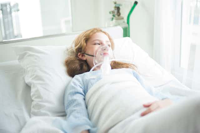 Girl with oxygen mask on lies in hospital bed