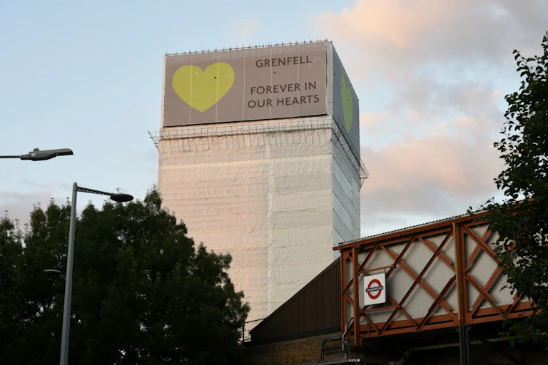 A high-rise building wrapped in white plastic sheets with a green heart and the message, Grenfell forever in our hearts.