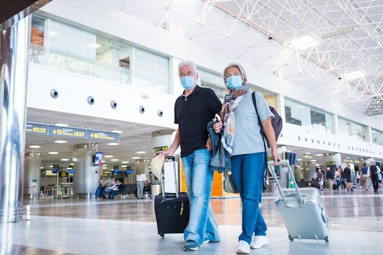 Older couple wheel suitcases through an airport.