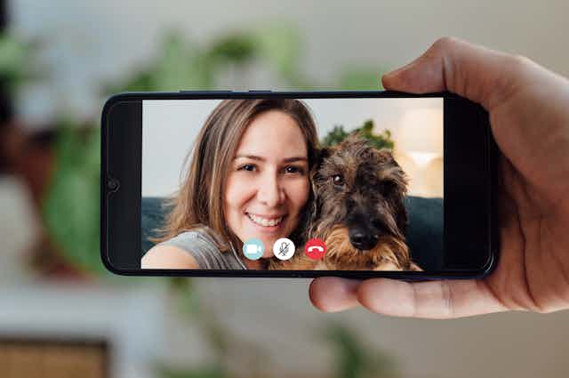 a hand holds a mobile phone with the screen showing a woman and a dog
