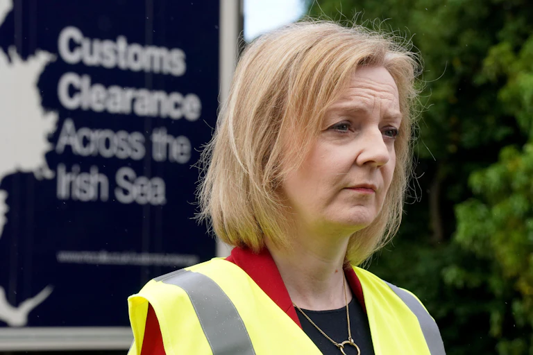UK foreign secretary Liz Truss looks forlorn in a high-vis vest. Behind her is a billboard reading Customs Clearance Across the Irish Sea.