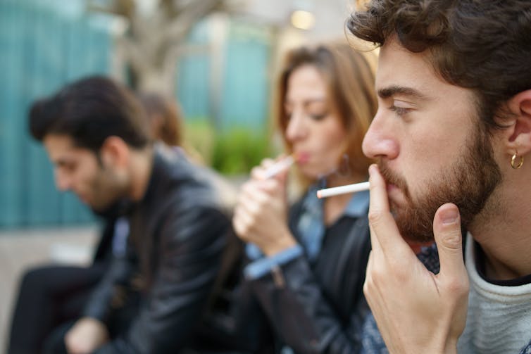 A young of three young people smoke cigarettes.