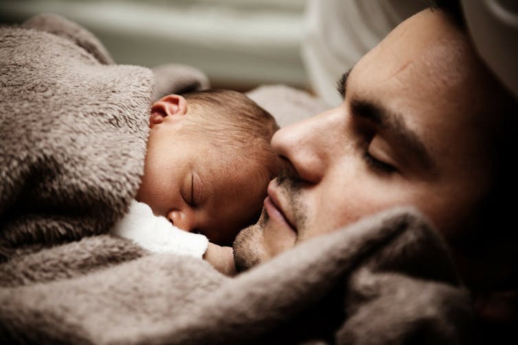 A newborn baby is seen sleeping on its father's chest.