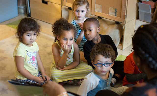 A group of children are seen listening to a story.