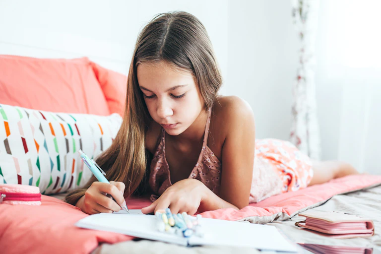 A girl lying on her bed drawing.