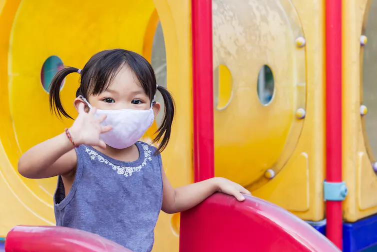 A young child is seen wearing a face mask at a playground.