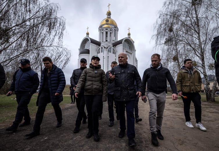 A row of people wearing dark jackets walk in front of a Ukrainian church
