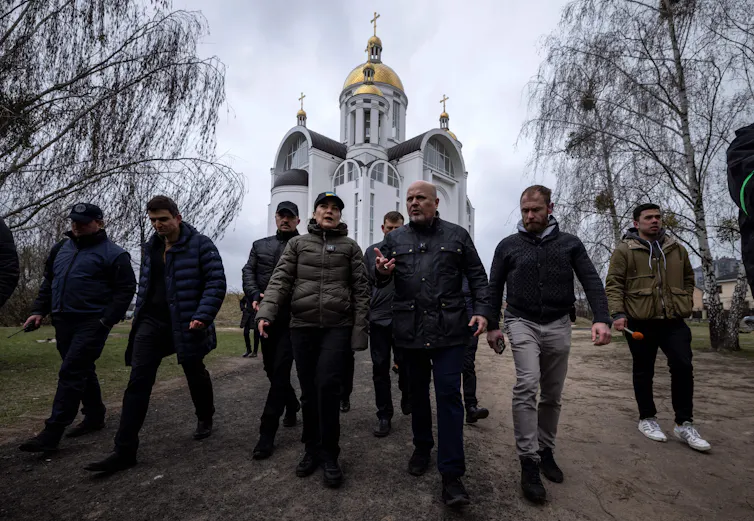 A row of people wearing dark jackets walk in front of a Ukrainian church