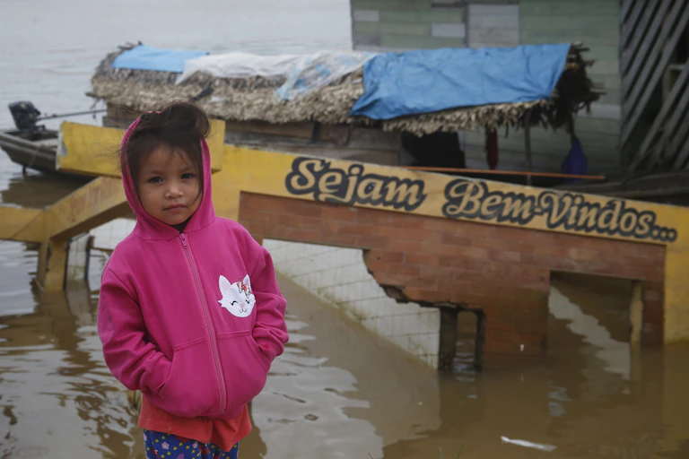 A child in a pink hoodie standing at the water's edge