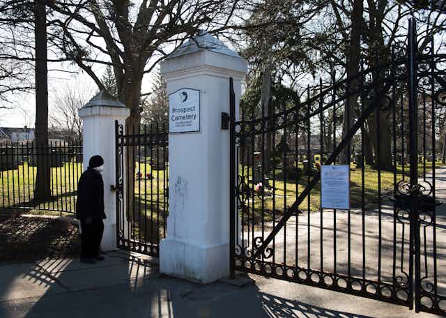 A cemetery with closed gates, a woman looks on