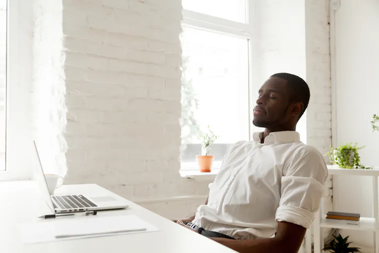 A man in a chair in white shirt, in a white room, with his eyes closed.