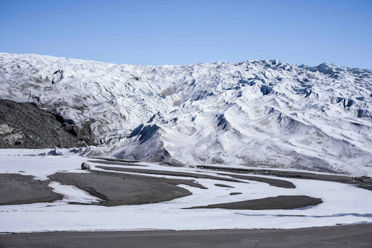 A wall of ice and snow with dark sand in front.