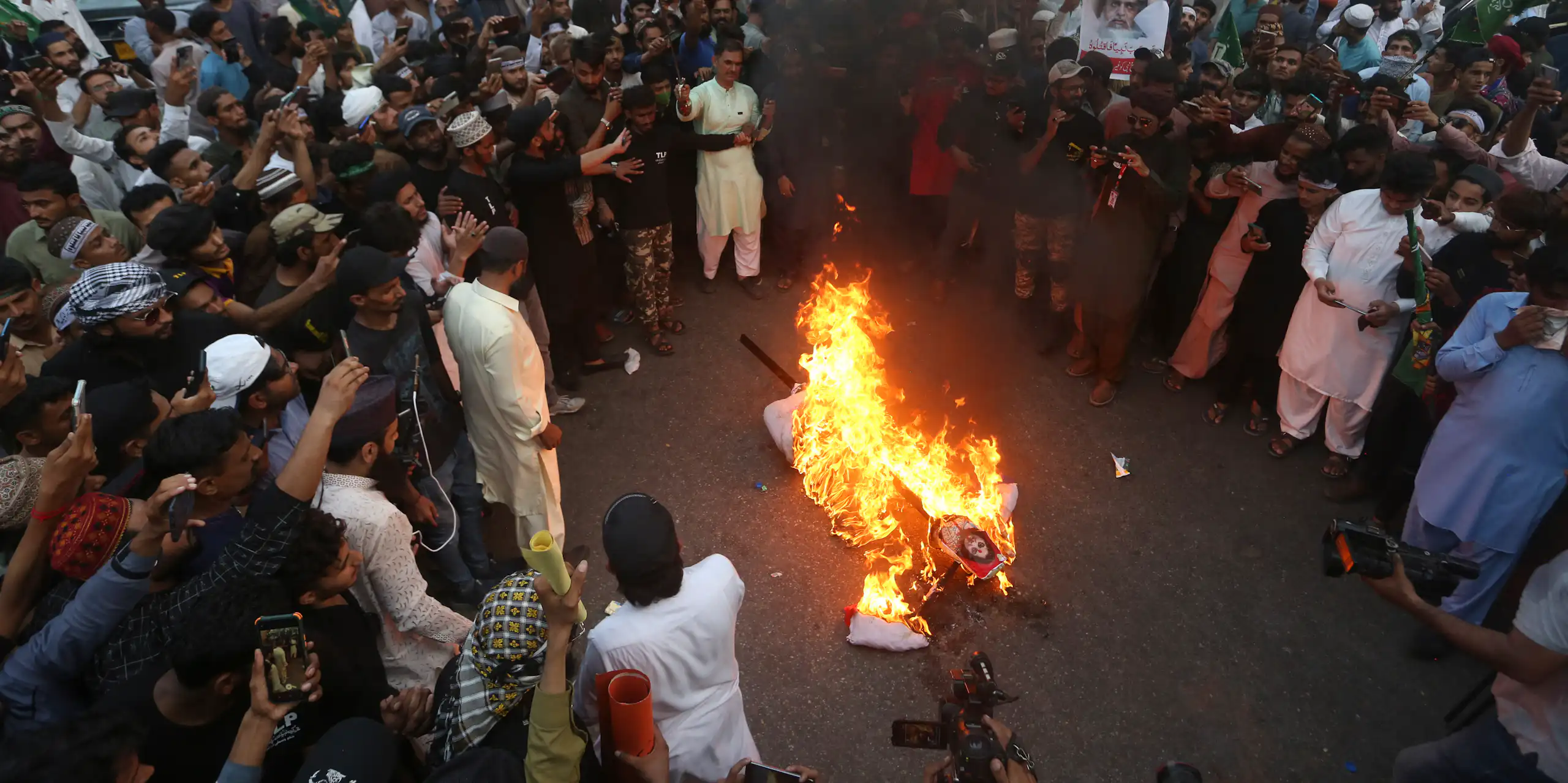 A large crowd gathers around a burning effigy during a demonstration.