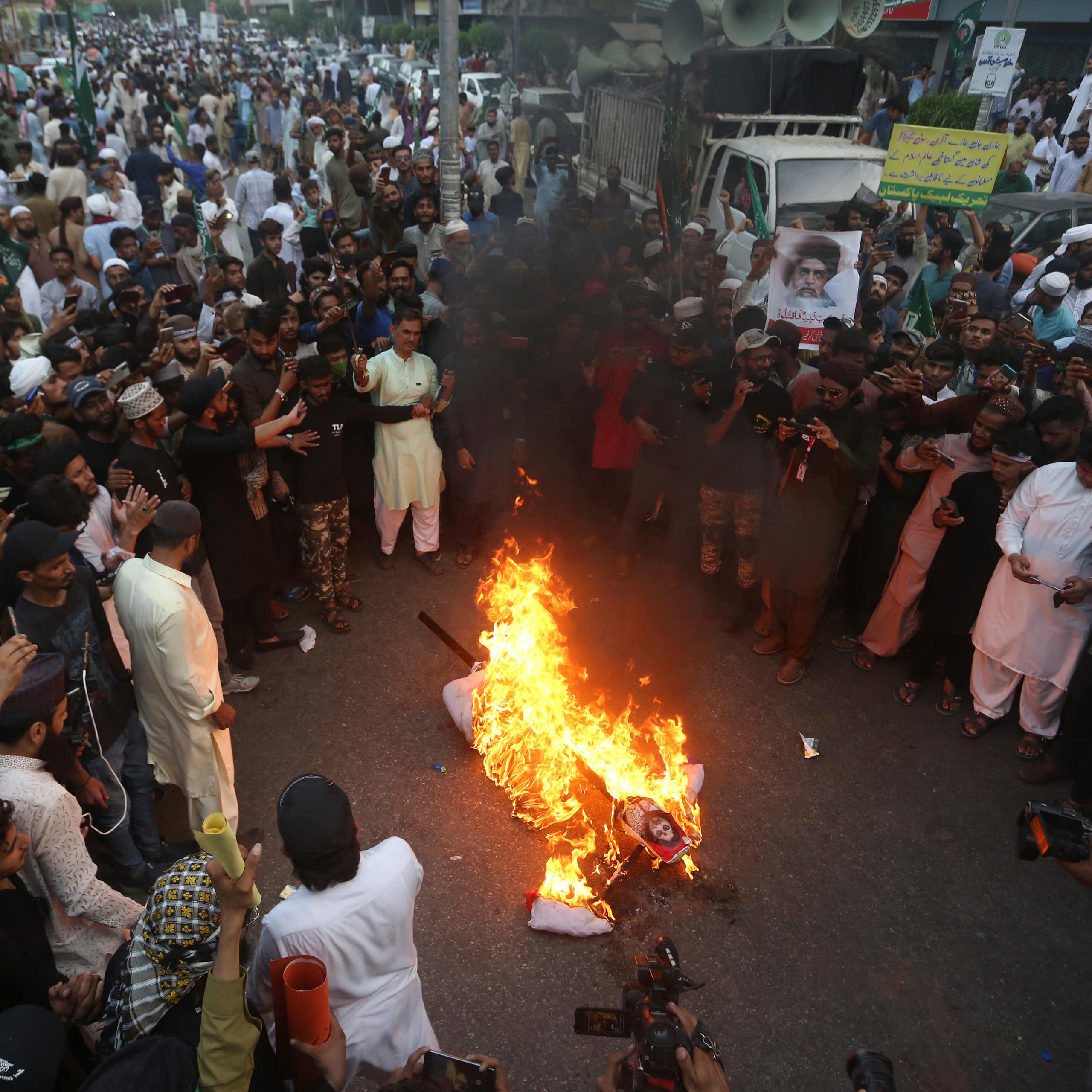 A large crowd gathers around a burning effigy during a demonstration.