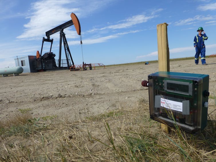 a recording device in the foreground and a pumpjack in the background