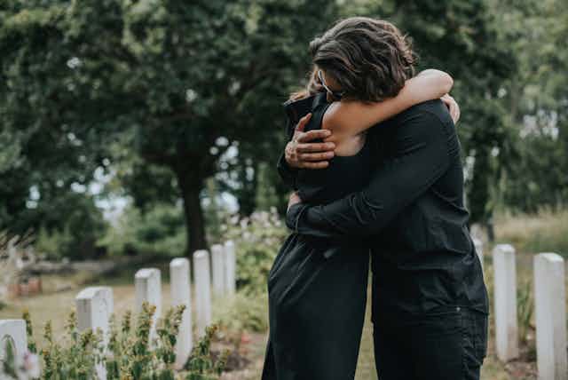 Two young adults wearing black hugging in cemetery