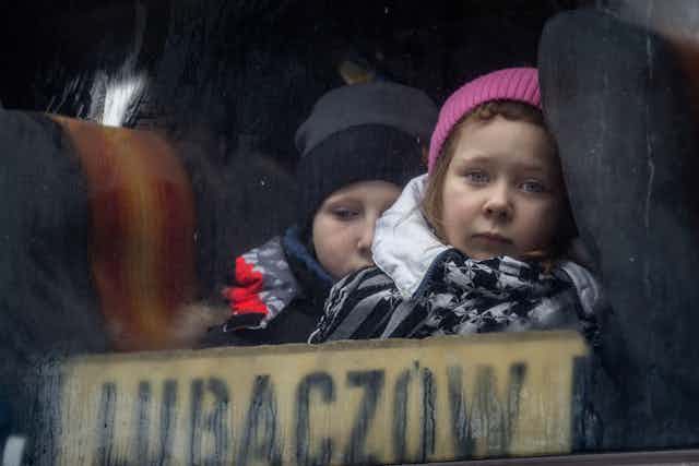 Two children, one in a pink hat, looking out of a bus window.