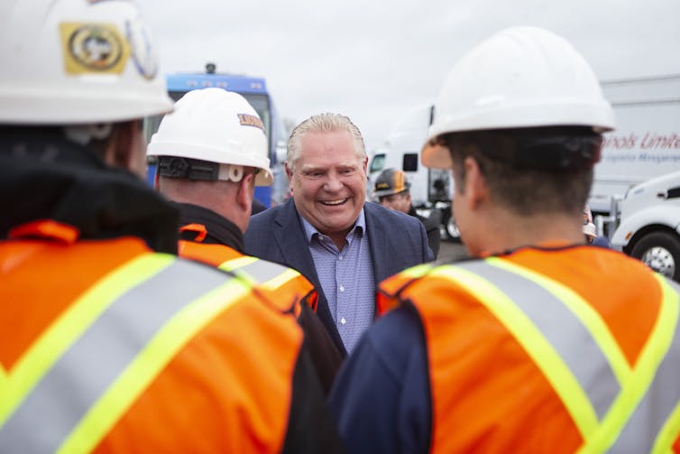 A man with slicked back blonde/grey hair shakes hands with construction workers.