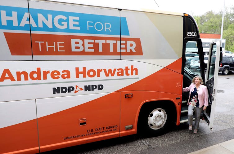 A woman steps off a campaign bus that says Change for the Better on the side.