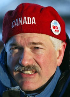 A man with a moustache wears a red Canada beanie.