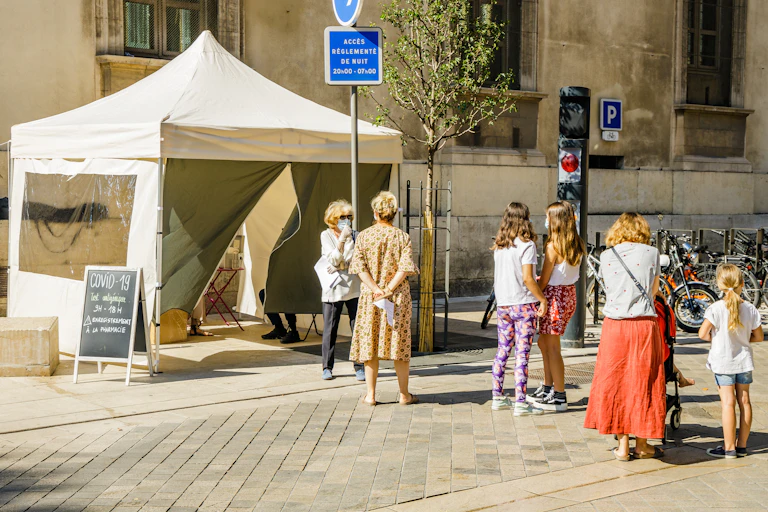 Une petite file de personnes attend, parfois masquées, devant une tente pour dépistage.
