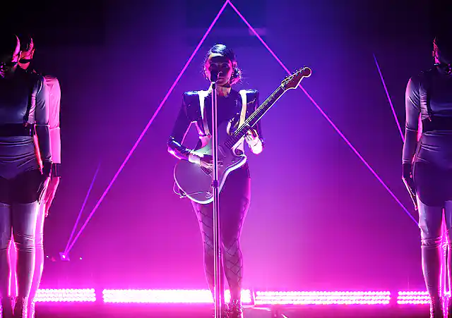 Woman plays guitar on stage bathed in pink light.