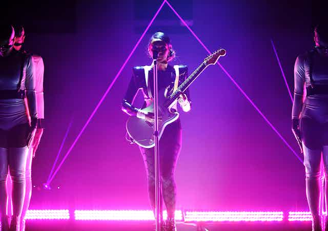 Woman plays guitar on stage bathed in pink light.