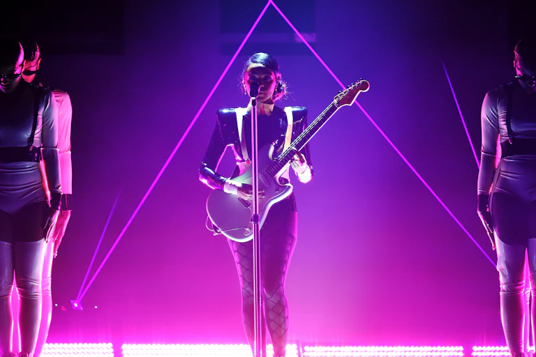 Woman plays guitar on stage bathed in pink light.