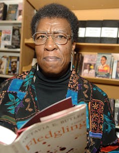 Woman in glasses holds book.