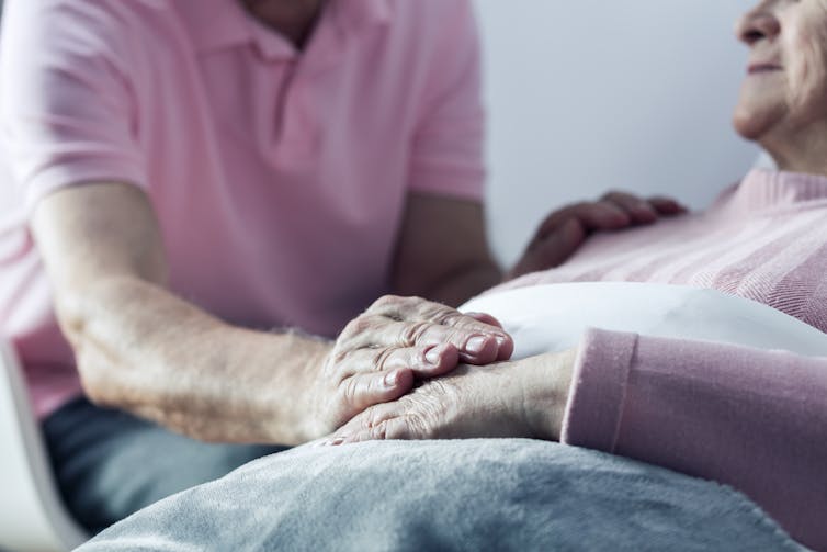 Man holds the hand of an older woman resting in bed