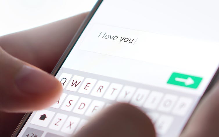 Close-up of man's fingers typing an'I love you' text message on a mobile phone.