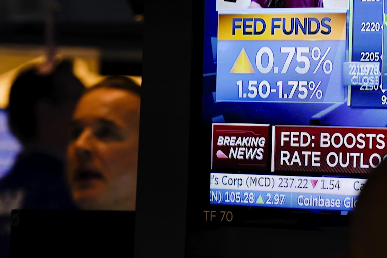The face of a white man looking off camera is shown next to tv screen showing news of 0.75 percentage point rate hike