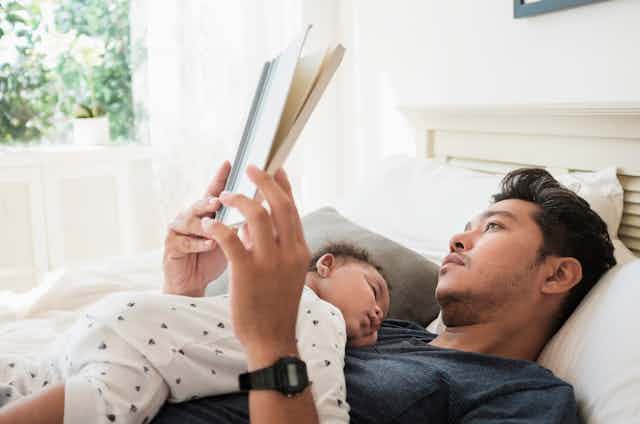 baby on belly sleeping on reclined reading man's chest