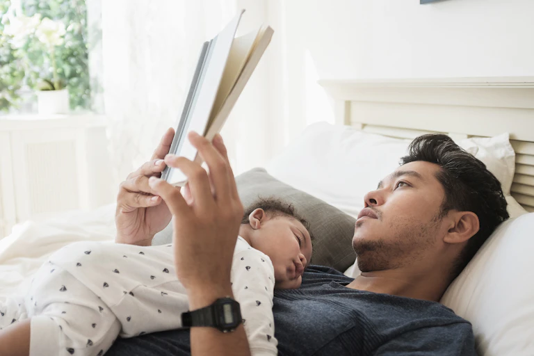 baby on belly sleeping on reclined reading man's chest