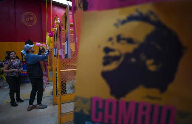 Supporters of Colombian left-wing presidential candidate Gustavo Petro paste banners onto an indoor fence.