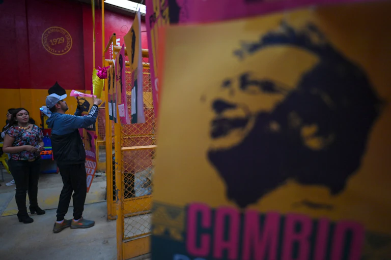 Supporters of Colombian left-wing presidential candidate Gustavo Petro paste banners onto an indoor fence.