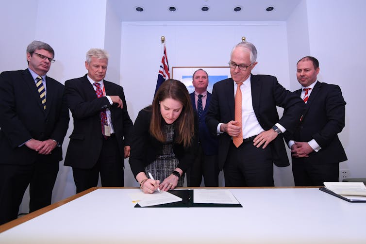 four men watch as woman signs paper