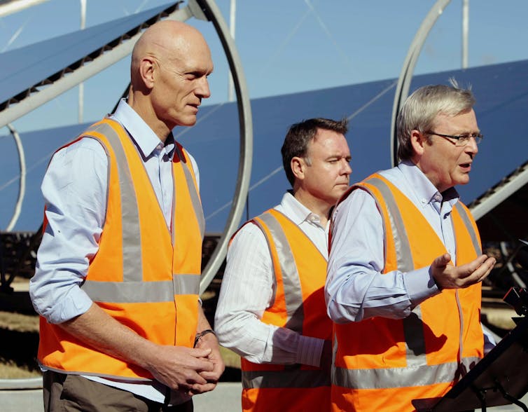 three men in orange vests in front of solar panels