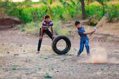 Two boys play cricket in a rural setting