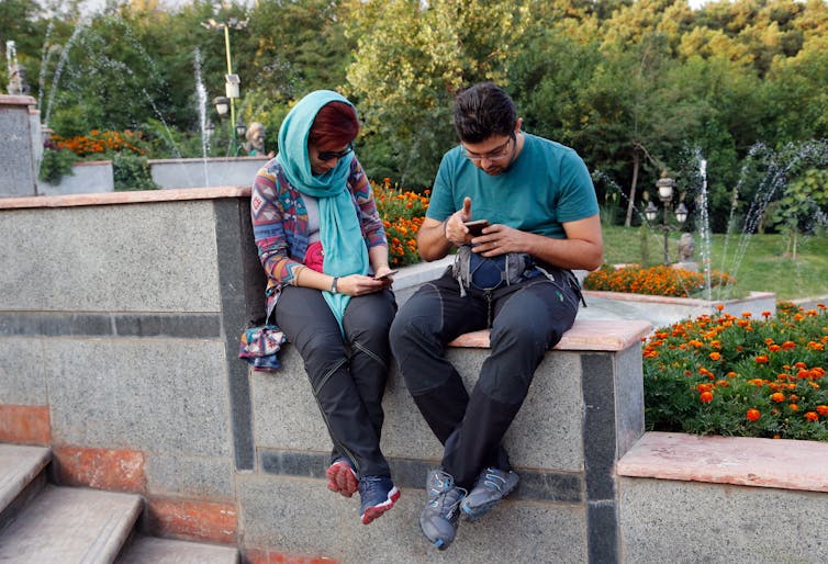 A young Iranian couple sit on a wall in a Tehran park playing ‘Pokemon Go’ on their smartphones.