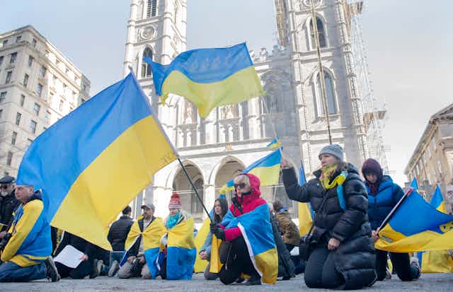 People wave Ukrainian flags as they kneel at a rally.