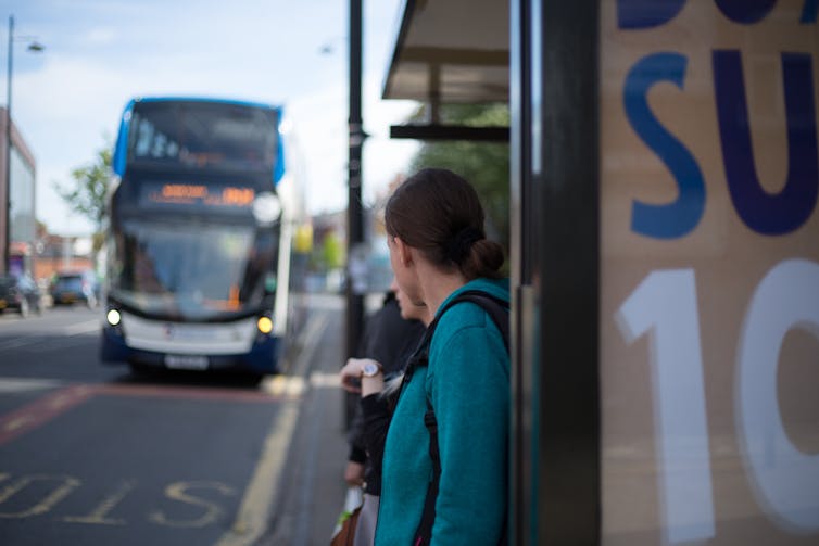 Woman stands at bus stop with bus approaching
