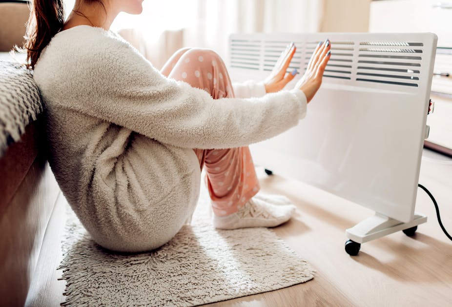 Une jeune femme met ses mains et pieds devant un radiateur