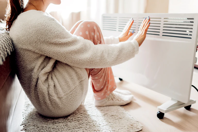 Une jeune femme met ses mains et pieds devant un radiateur