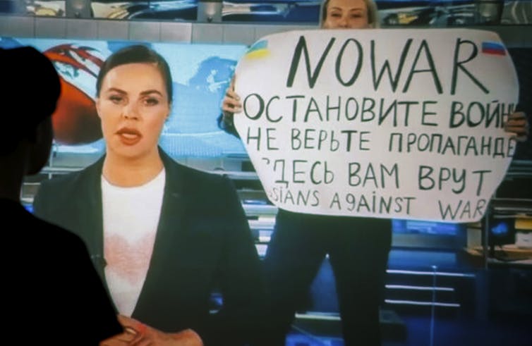 Screenshot of Russia's Channel 1 network news bulletin with journalist Marina Ovsyannikova holding up an anti-war message in the background.