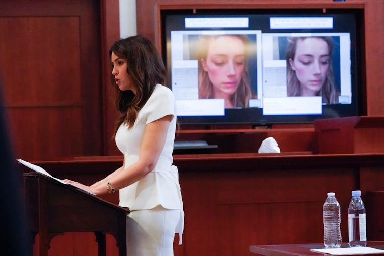 Johnny Depp's lawyer, Camille Vasquez, stands in a white dress, in front of two images of Amber Heard that show bruising on her face